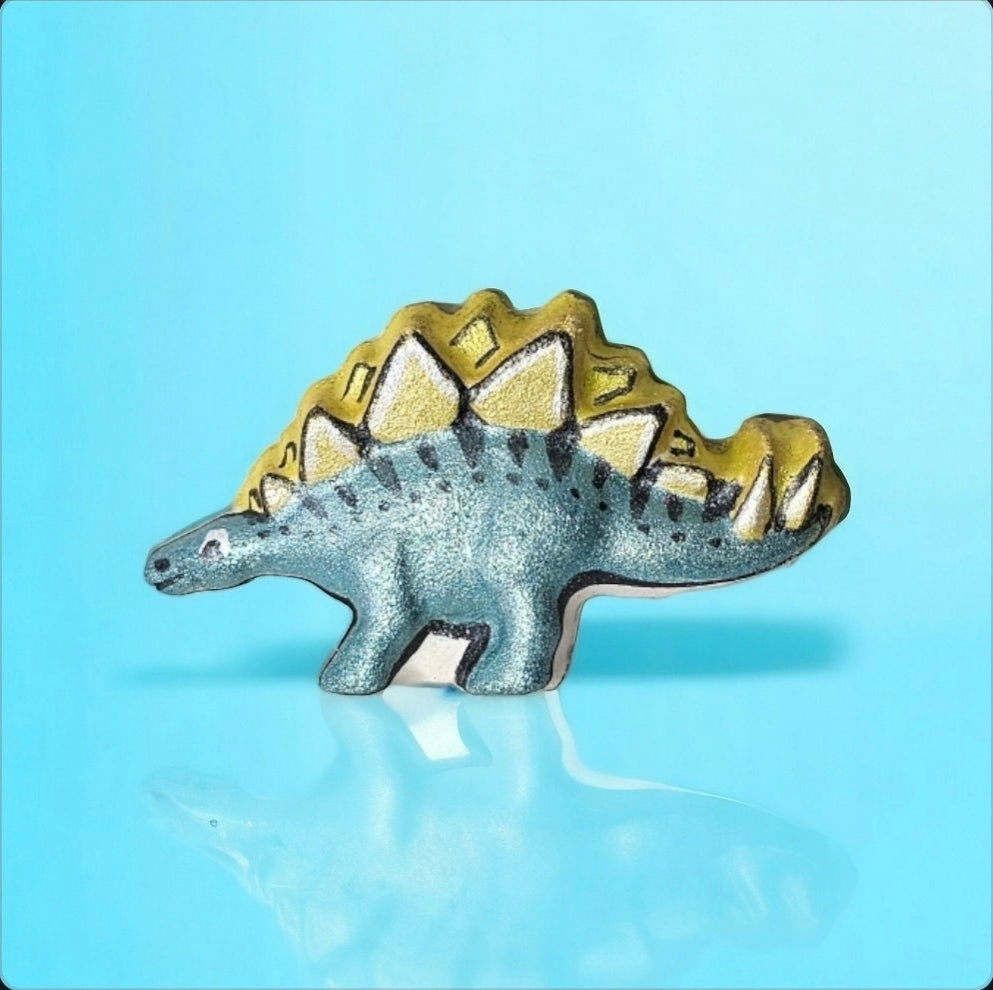Dinosaur-shaped bath bomb with teal and yellow colour on a light blue background